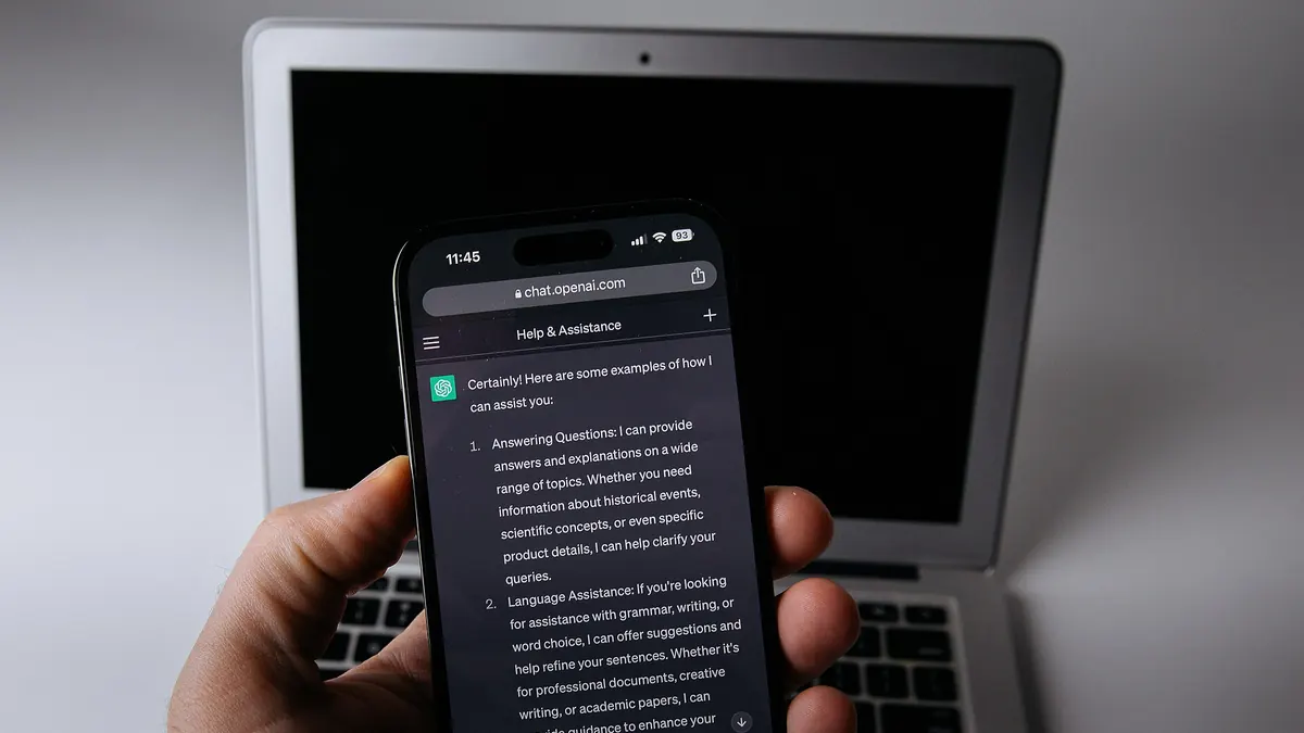 Aplicación ChatGPT en un teléfono junto a un portátil, fotografía de archivo de 2023. No presenta una pantalla real de la función de bloqueo de chats.